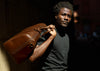 man holding brown leather weekend bag by handles